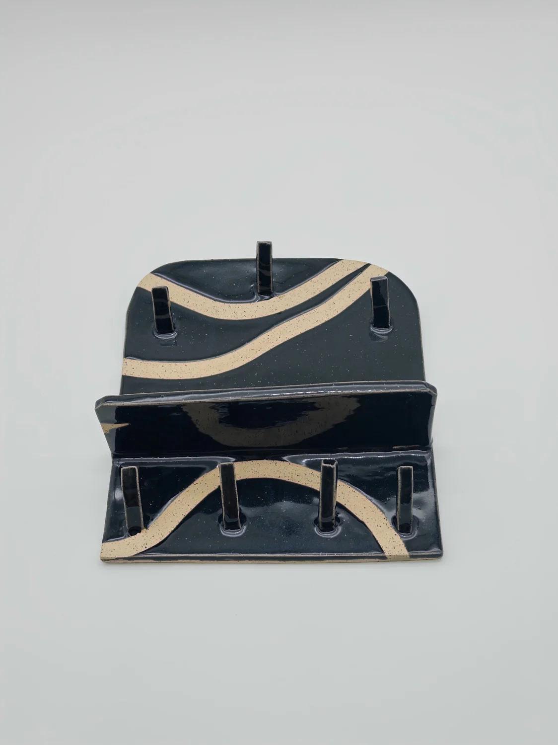 Black rectangular ceramic stand with cream curved stripes and upright pegs, view 2