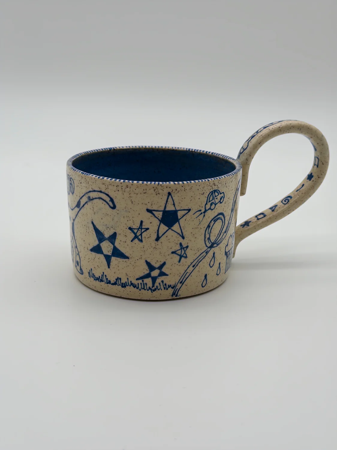 Cream mug with blue doodles, a blue interior, and a curved handle, view 2